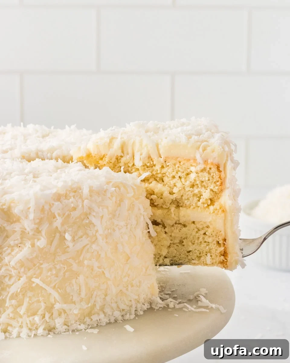 A delectable slice of gluten-free coconut cake being lifted from a beautifully frosted layer cake, generously adorned with shredded coconut, showcasing its moist texture and inviting appeal.