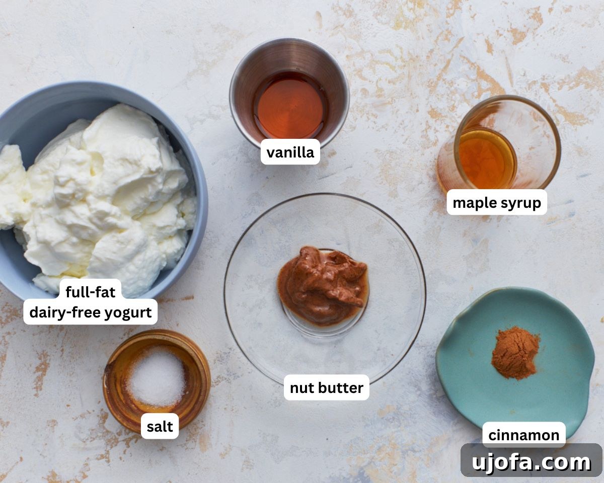 Velvety Vegan Fruit Dip 4 A selection of ingredients laid out for dairy-free fruit dip: a bowl of yogurt, a jar of nut butter, maple syrup, vanilla extract, cinnamon, and a salt grinder.
