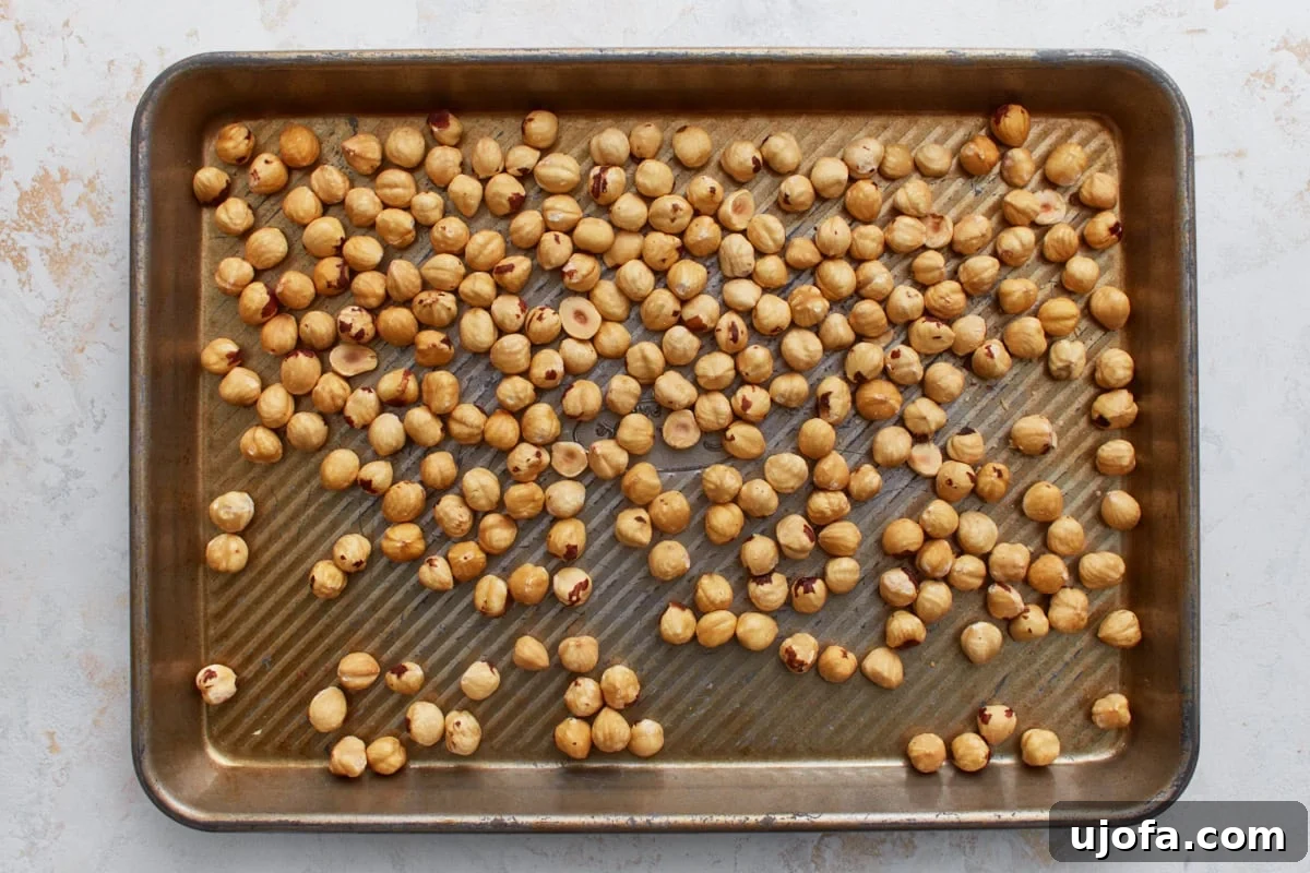 Blanched hazelnuts spread in an even layer on a baking sheet, ready for roasting in the oven to enhance their flavor for vegan Nutella.