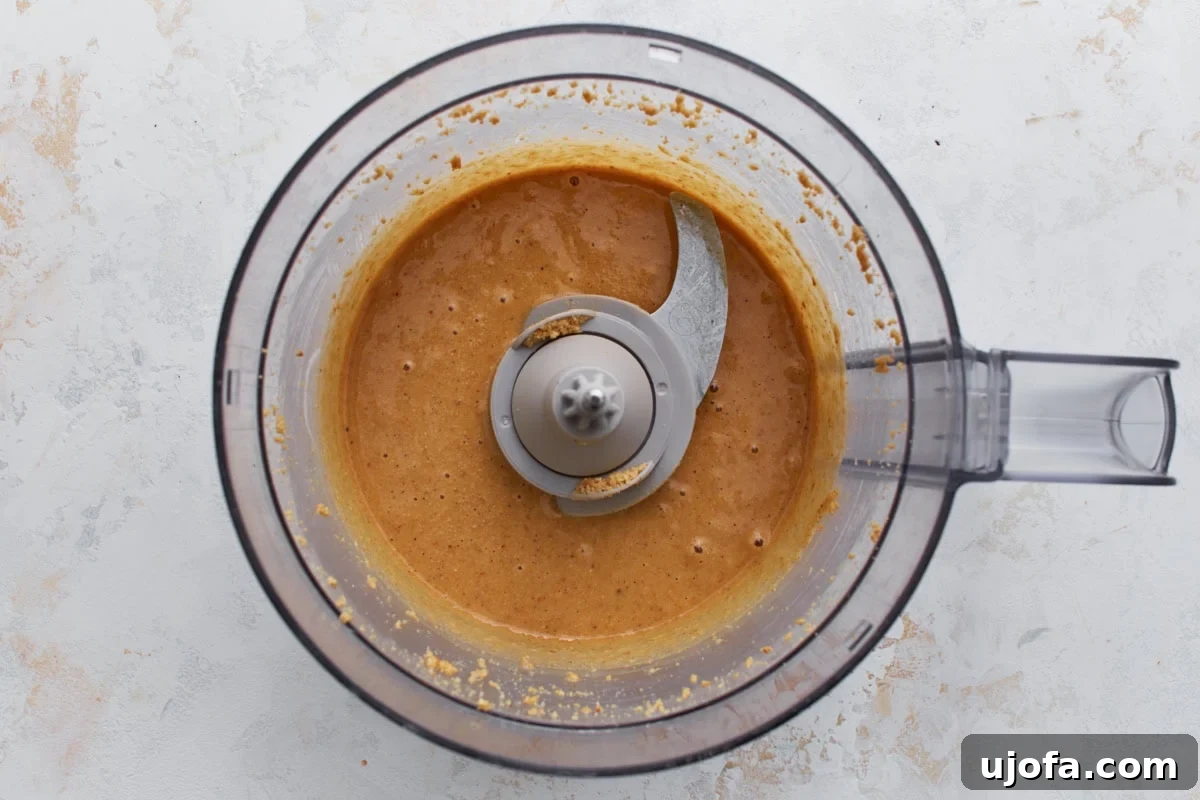 Warm, roasted hazelnuts being blended in a food processor, starting to form a thick, creamy nut butter, demonstrating the transformation from whole nuts to spreadable consistency.