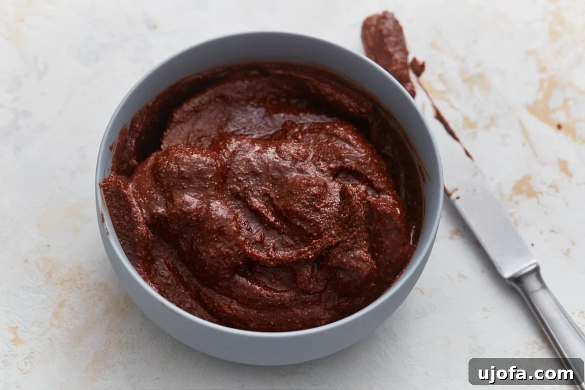 A bowl of freshly made homemade vegan Nutella, with a knife resting in it, showcasing its rich, smooth, and easily spreadable texture, ready to be enjoyed.