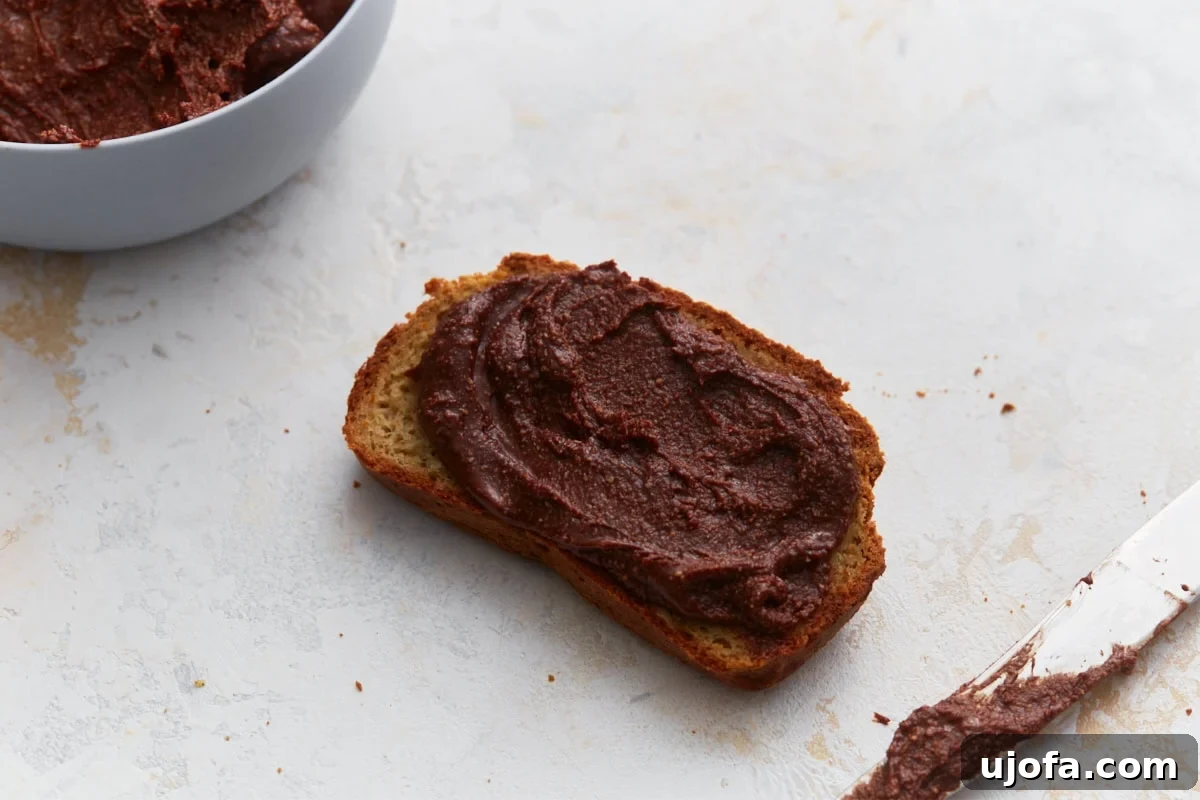 A slice of golden brown toast generously spread with rich, thick, and creamy homemade vegan Nutella, inviting a delicious bite.