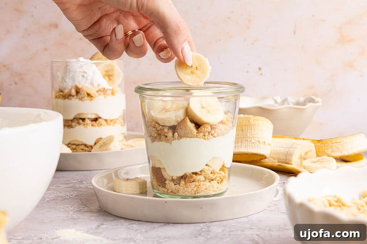Protein-Packed Banana Pudding Cups for Muscle Fuel 6 a hand adding ingredients to layers of banana pudding in a cup