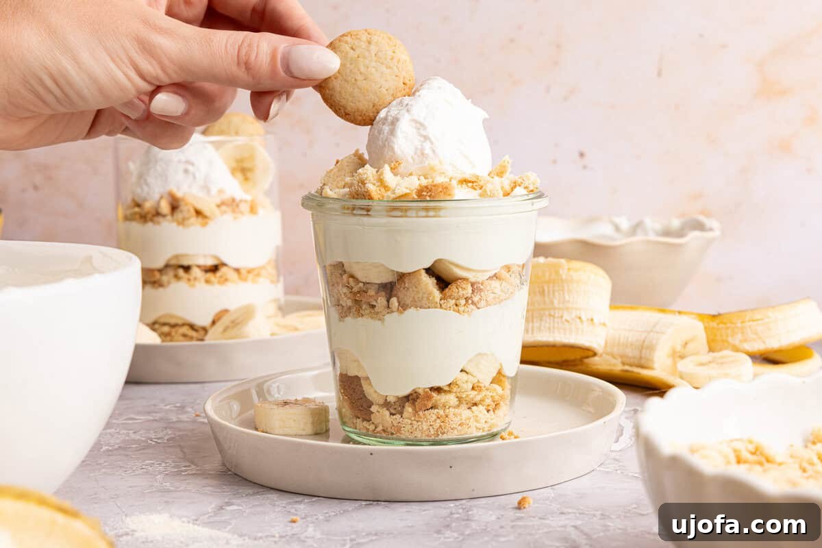 Protein-Packed Banana Pudding Cups for Muscle Fuel 7 a hand placing a vanilla wafer on top of a cup of banana pudding
