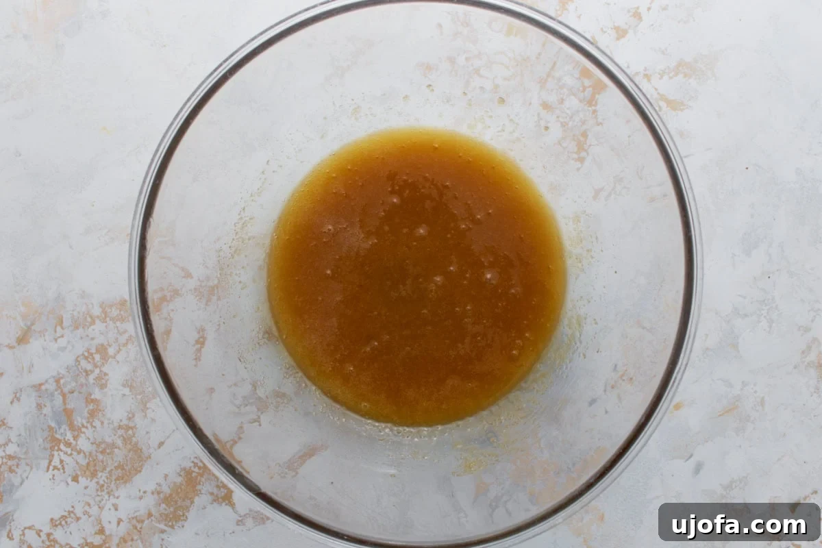 Melted butter and sugars combined in a clear glass mixing bowl