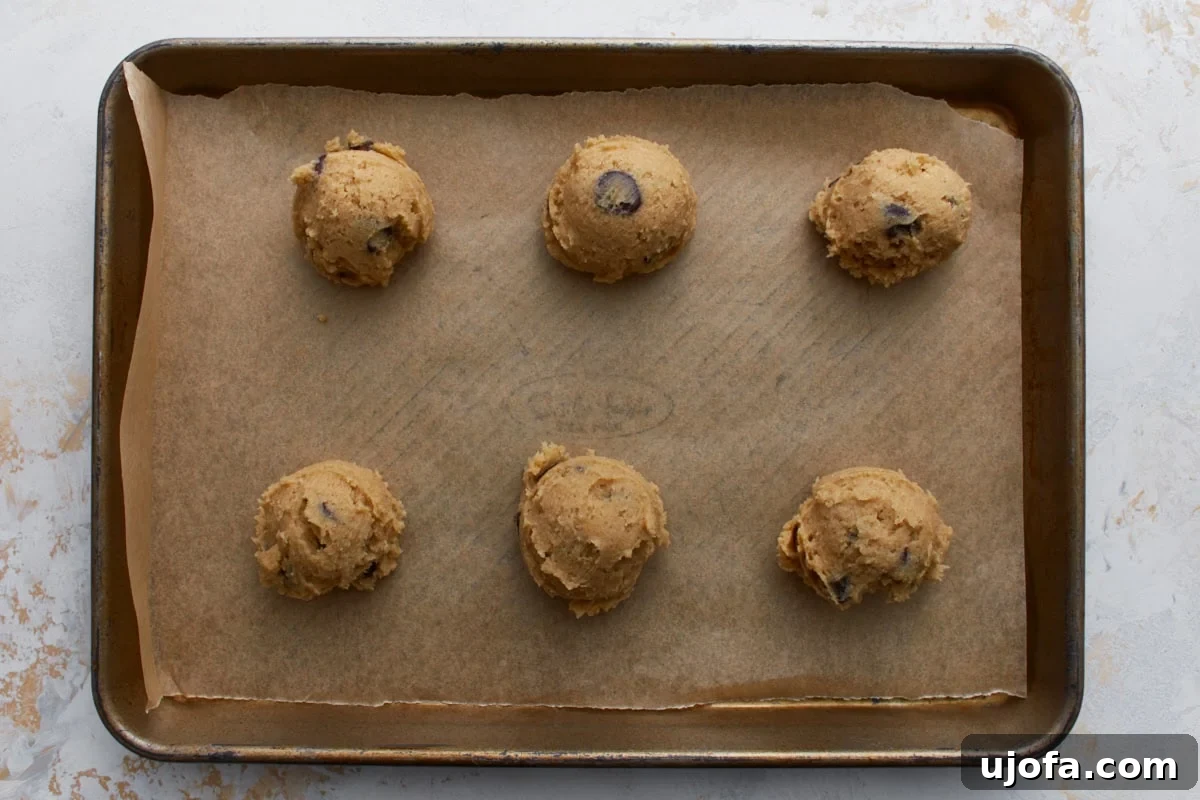 Scoops of buckwheat chocolate chip cookie dough portioned onto a parchment lined baking sheet before baking