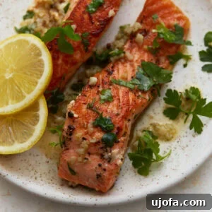 Keto Salmon in Garlic Butter Lemon Sauce 3 Keto salmon fillets with garlic butter sauce, fresh parsley, and lemon slices on a plate