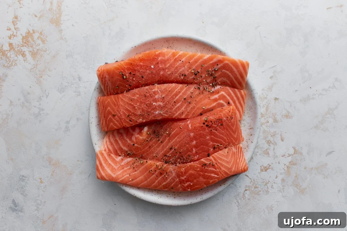 Keto Salmon in Garlic Butter Lemon Sauce 5 Raw salmon fillets seasoned with salt and black pepper on a white plate