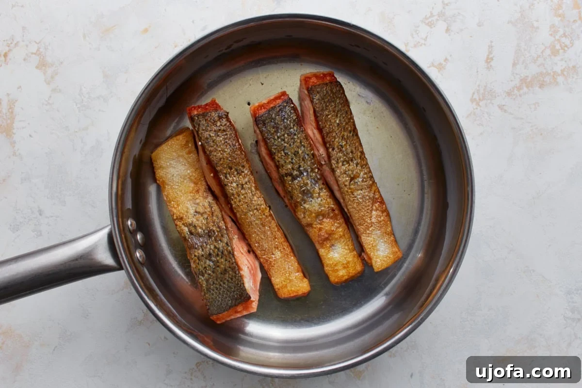 Keto Salmon in Garlic Butter Lemon Sauce 6 Salmon fillets cooking skin-side down in a skillet with crispy golden skin