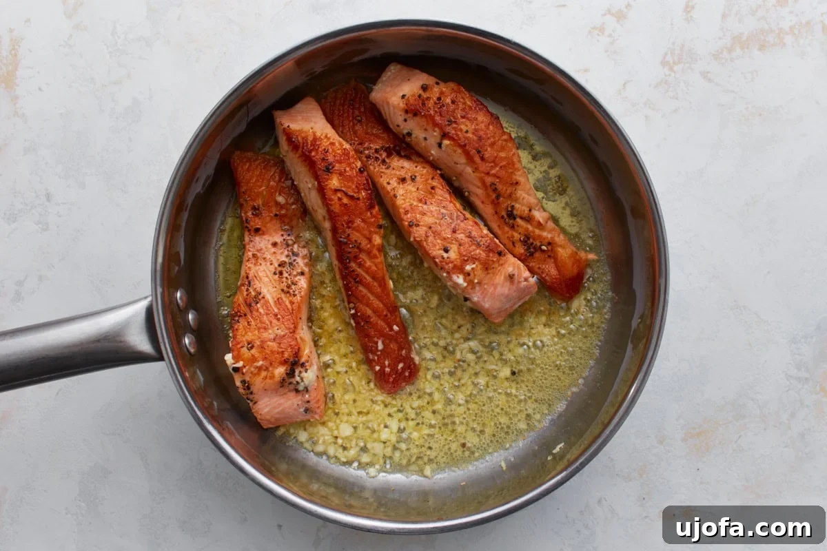 Keto Salmon in Garlic Butter Lemon Sauce 7 Seared salmon in a pan with melted butter and minced garlic
