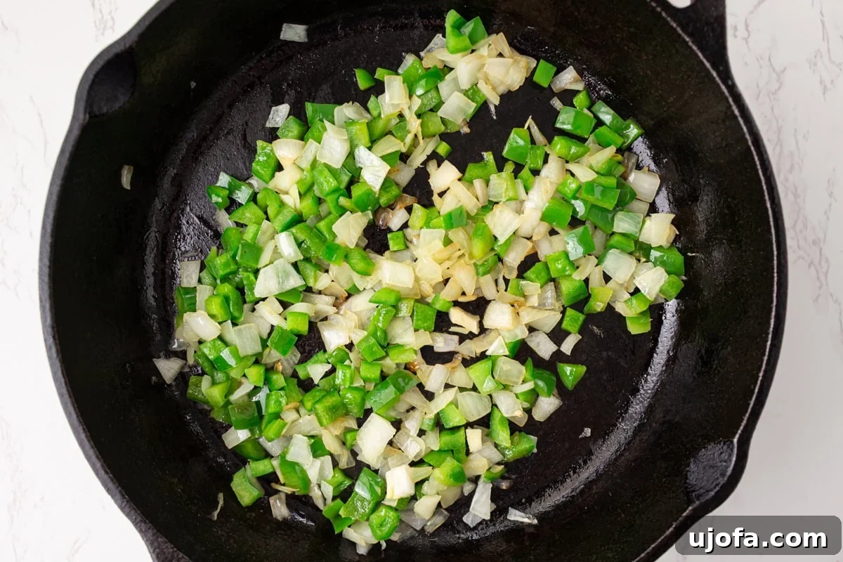 Diced green bell pepper and onion cooking in a cast iron skillet
