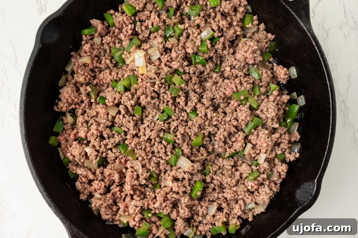 Ground beef cooking with softened peppers and onions in a skillet
