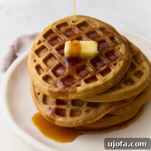Crispy Oat Flour Waffles Recipe for Fluffy Homemade Waffles 3 Stack of oat flour waffles topped with butter and maple syrup on a white plate.
