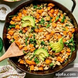 One-Skillet Turkey and Sweet Potato Hash Recipe 9 an egg-free breakfast hash with sweet potatoes, ground turkey, and spinach in a cast iron skillet topped with avocado with a wooden spoon