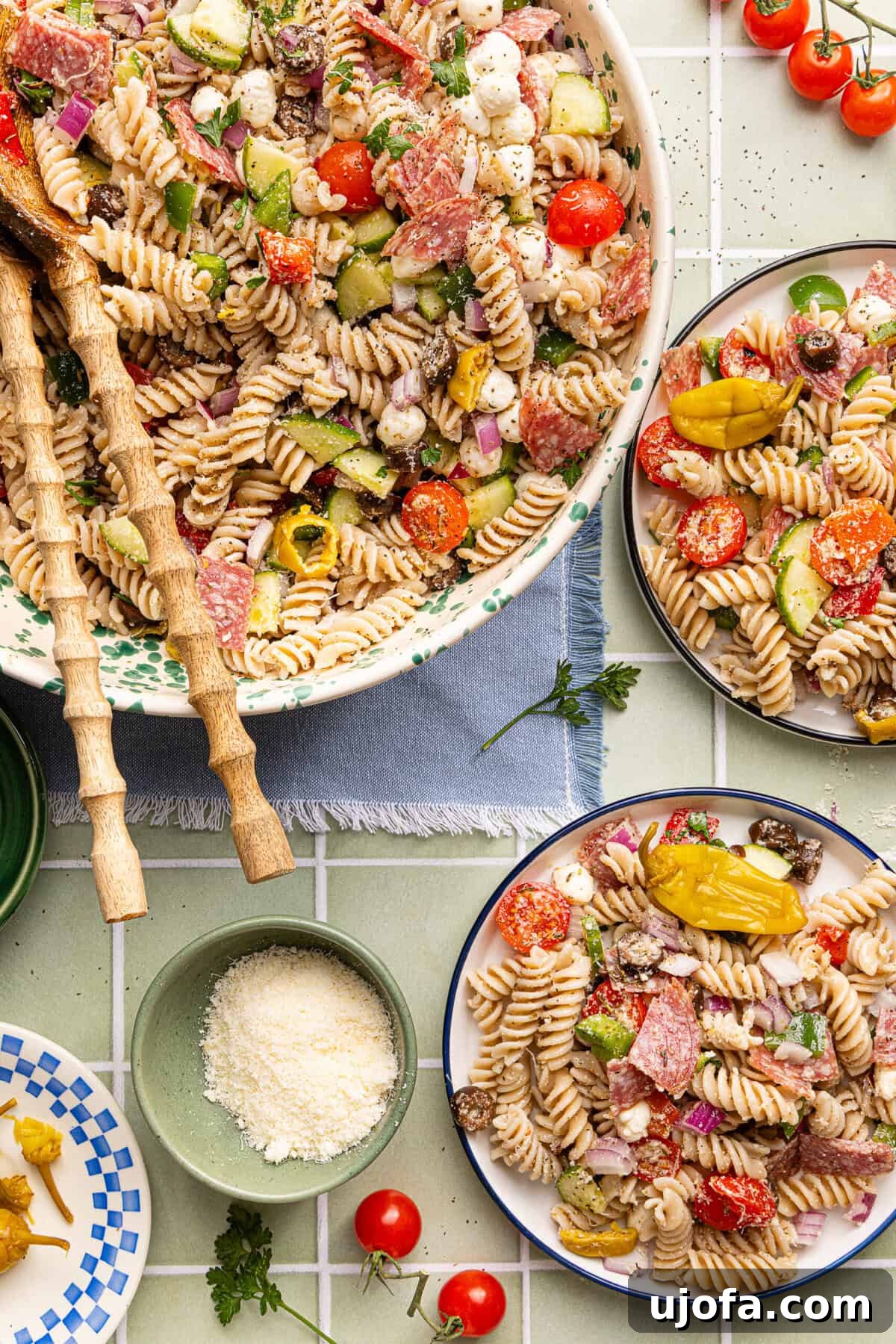 Gluten-Free Italian Pasta Salad Recipe for Flavorful Picnics 2 Gluten free pasta salad served in a decorative bowl with wooden serving spoons, alongside two plates of pasta salad and a small bowl of grated parmesan cheese.
