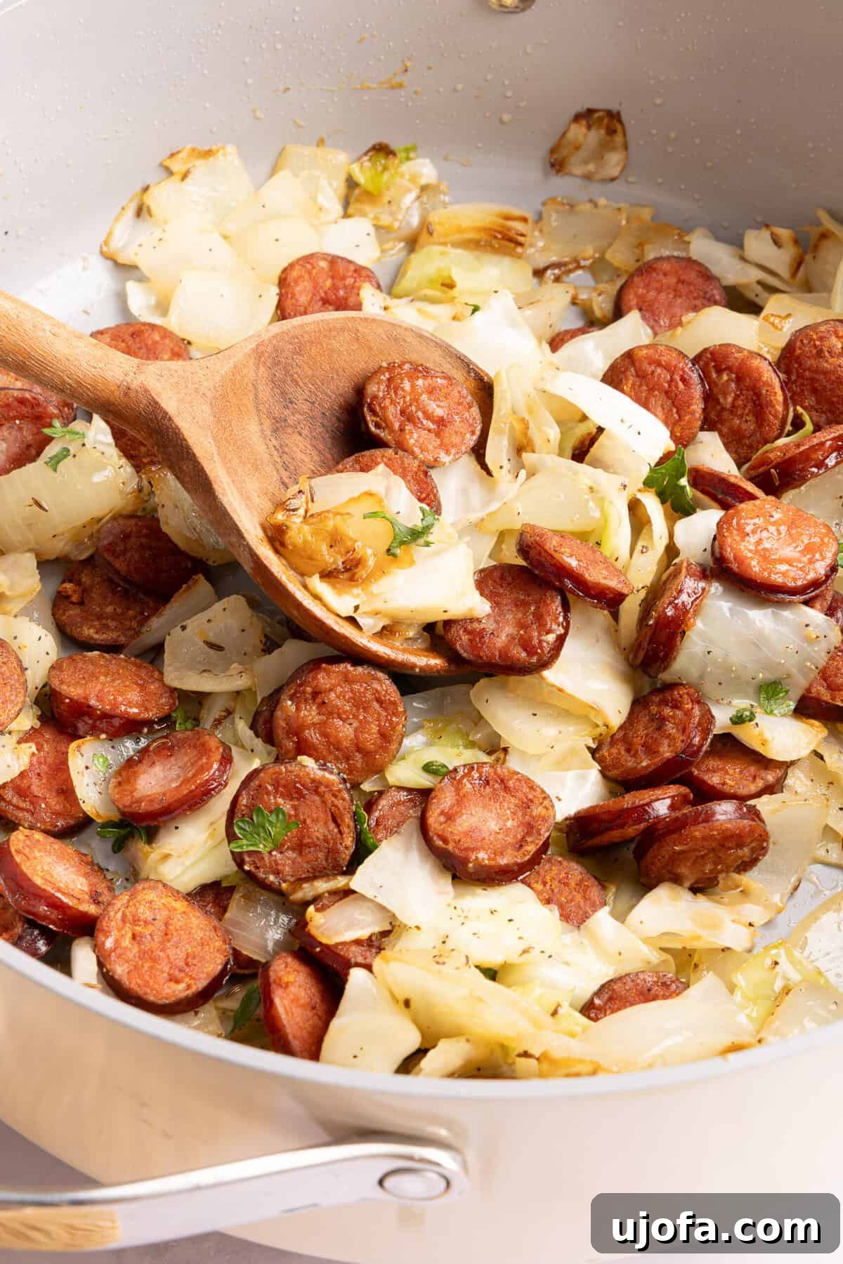 kielbasa and cabbage in a skillet with a wooden spoon