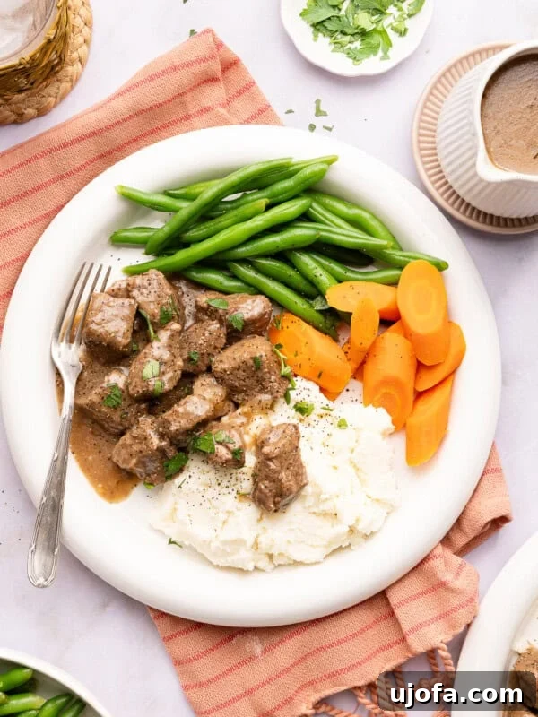 beef tips over mashed potatoes with green beans and carrots on a plate