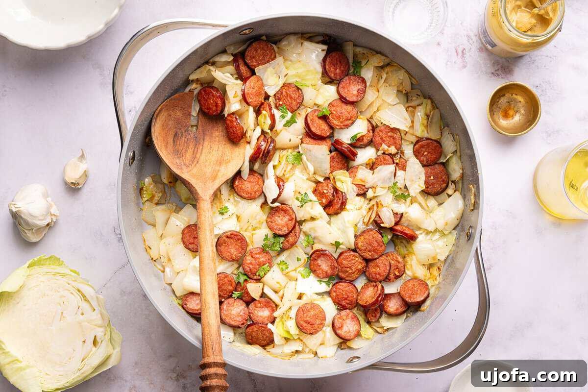 sausage and cabbage in a skillet with a wooden spoon