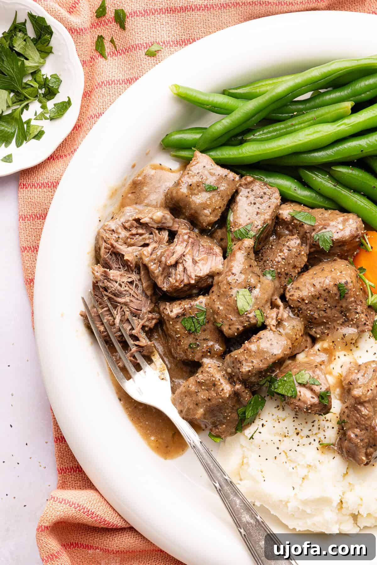 beef tips with gravy over mashed potatoes with green beans on a plate