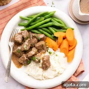 beef tips over mashed potatoes with green beans and carrots on a plate