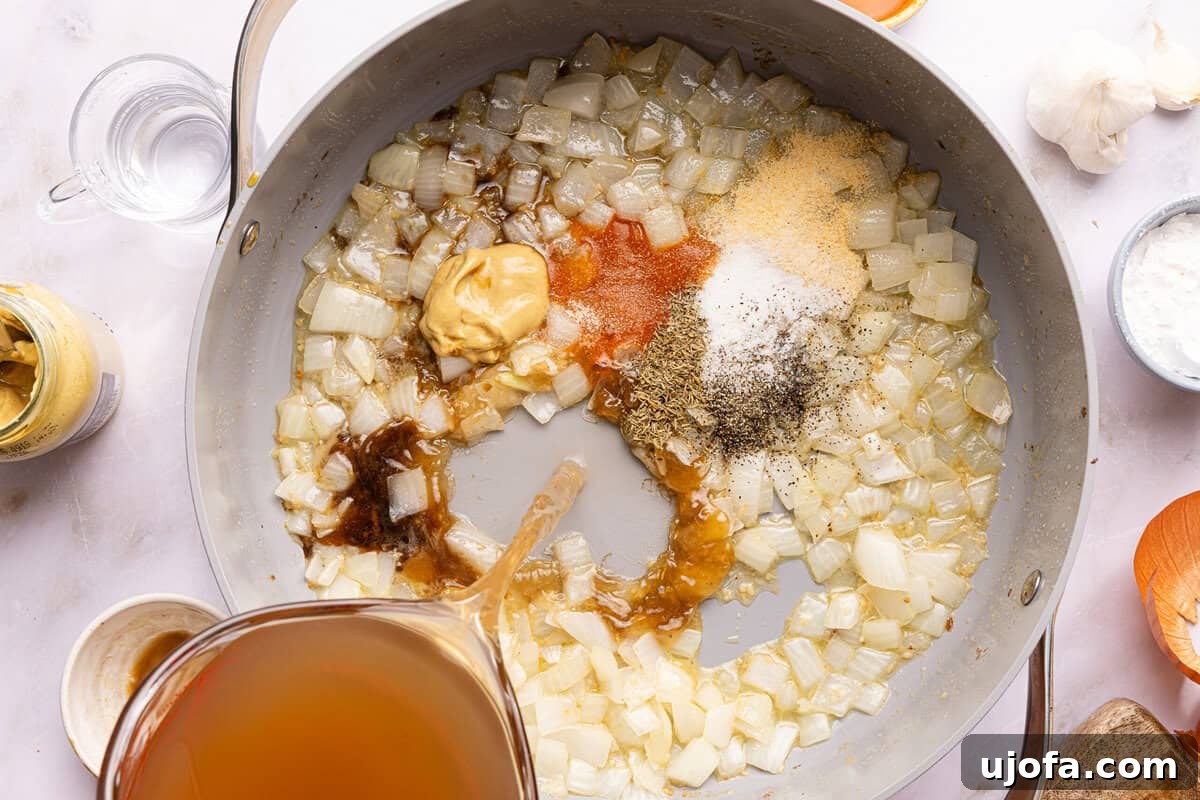 onions and spices in a pan with broth being poured in