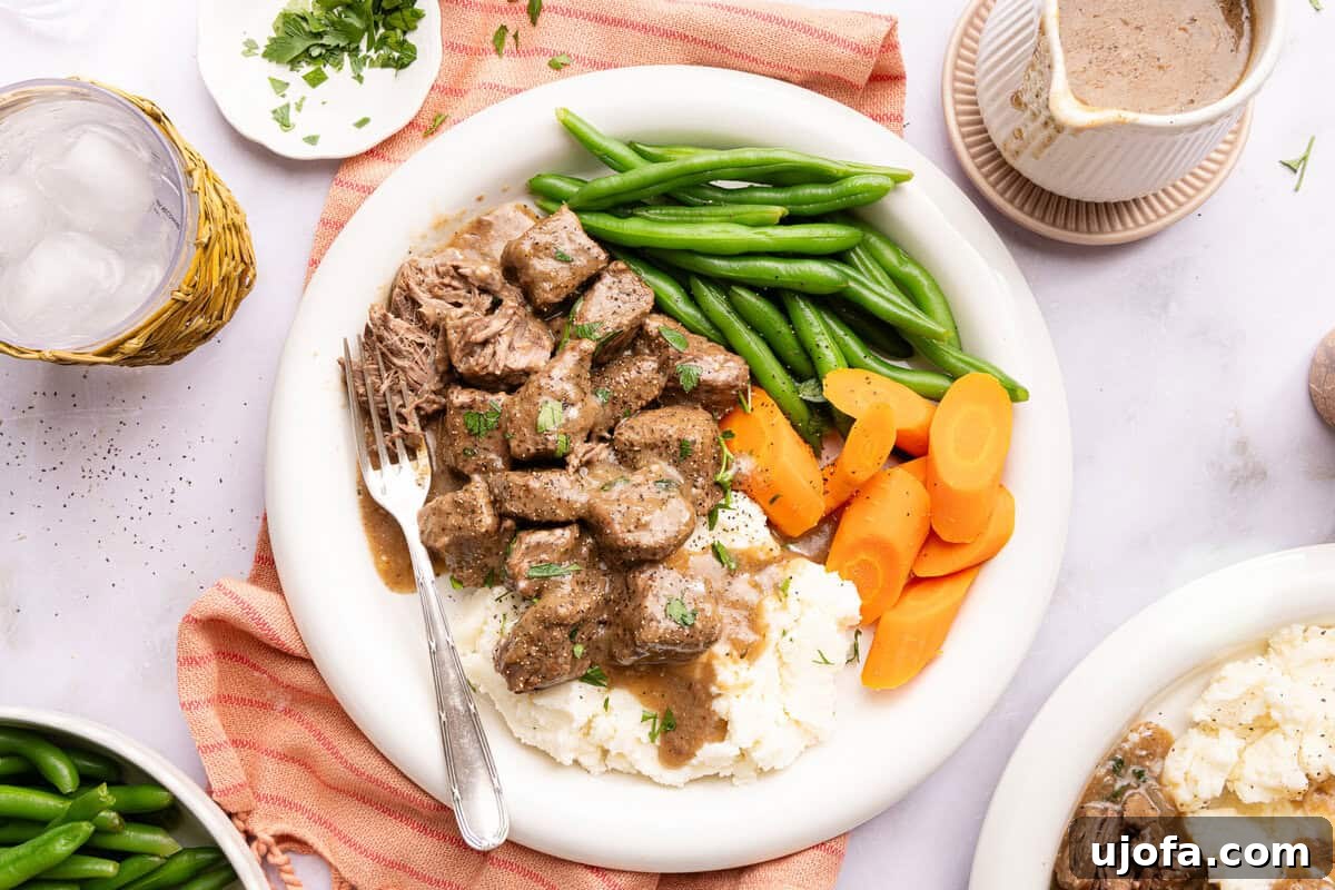a plate of beef tips over mashed potatoes with vegetables