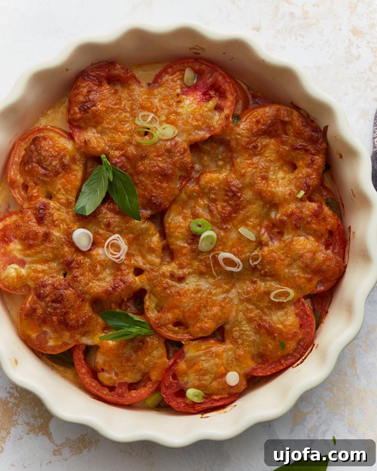 Overhead view of baked crustless tomato pie topped with melted cheese, fresh basil, and sliced green onions in a white pie dish.