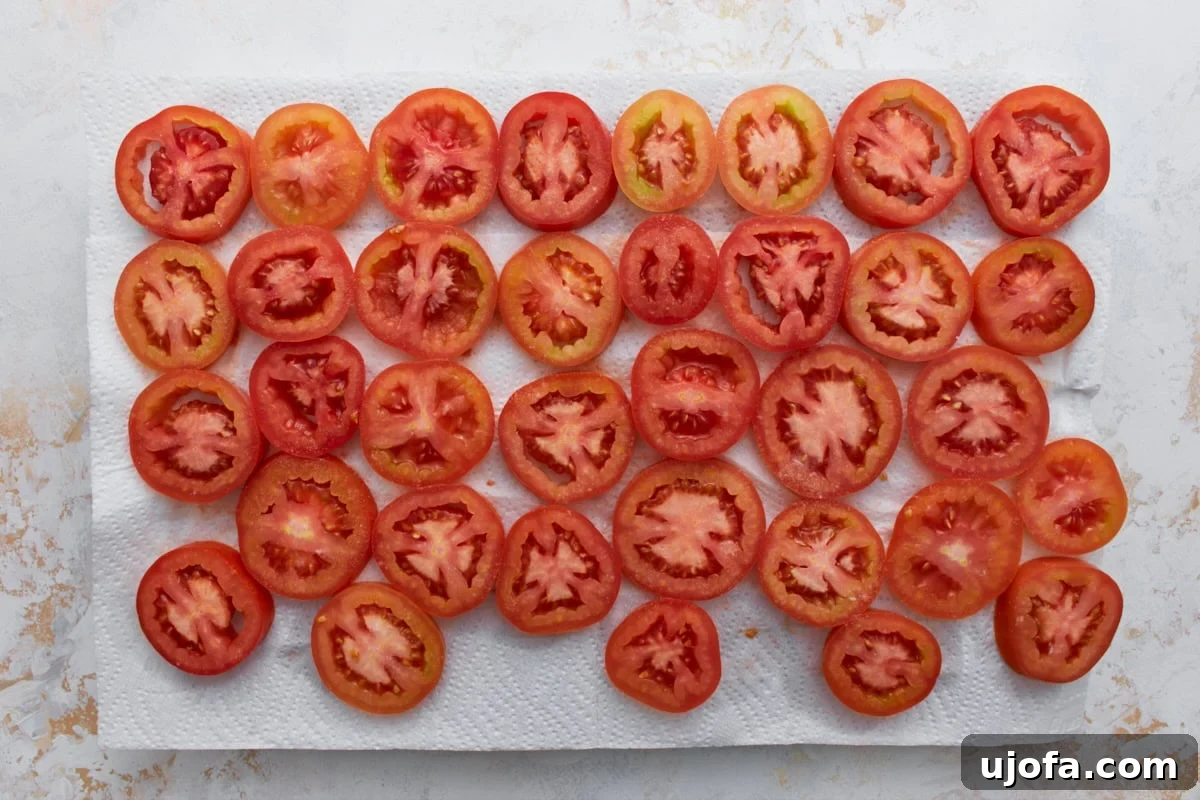 Sliced fresh tomatoes arranged on paper towels to drain excess moisture before making crustless tomato pie.