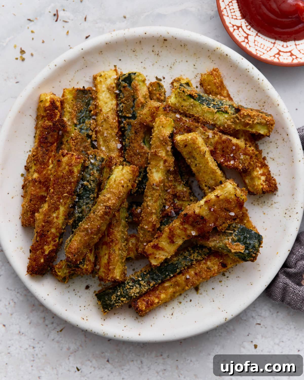Crispy baked keto zucchini fries coated in Parmesan and almond flour served on a white plate with a side of ketchup.