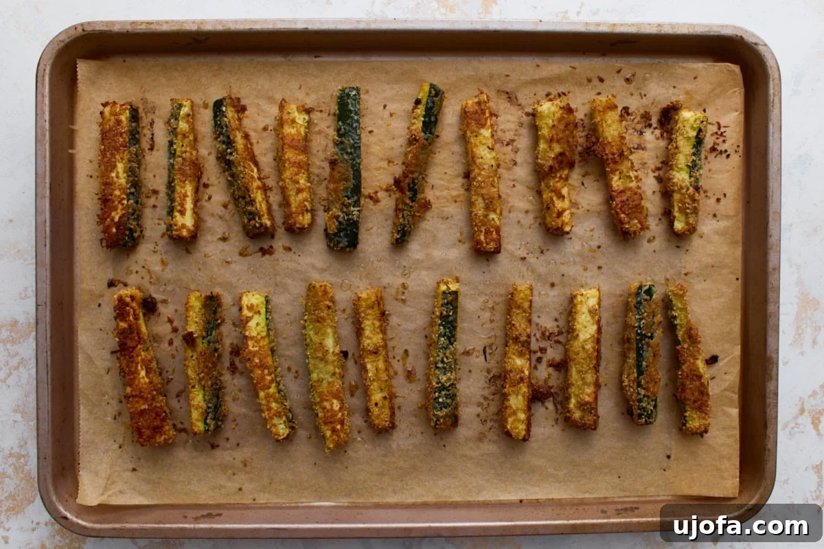 Golden brown baked keto zucchini fries on a parchment-lined baking sheet after roasting until crispy.