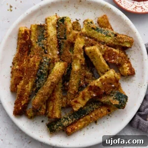 Crispy baked keto zucchini fries coated in Parmesan and almond flour served on a white plate with a side of ketchup.