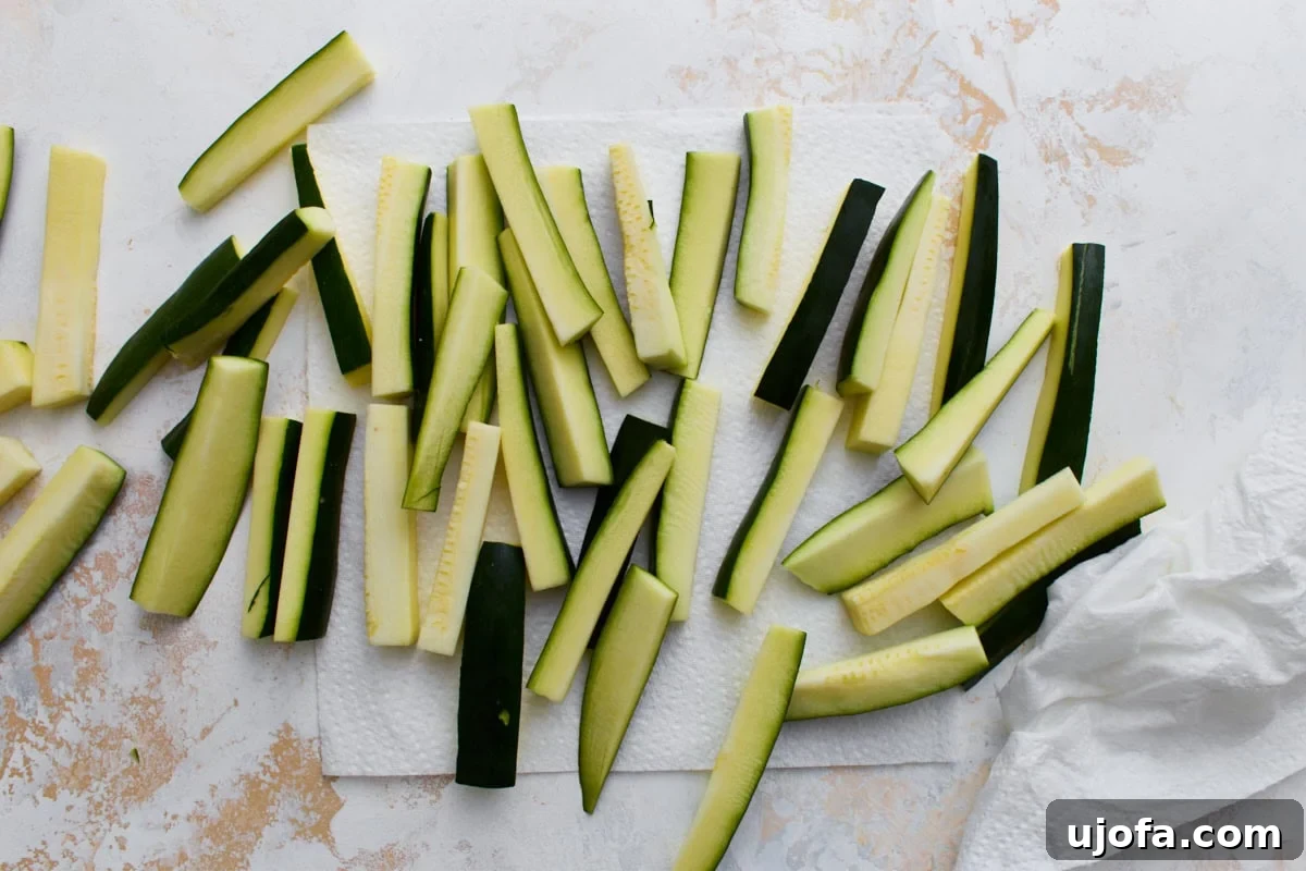 Fresh zucchini cut into fry-shaped sticks drying on paper towels before breading.