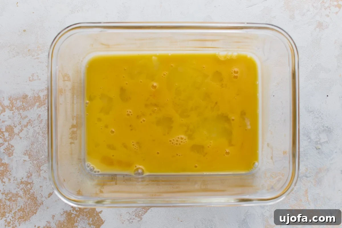 Beaten egg in a glass container prepared for coating the zucchini fries.
