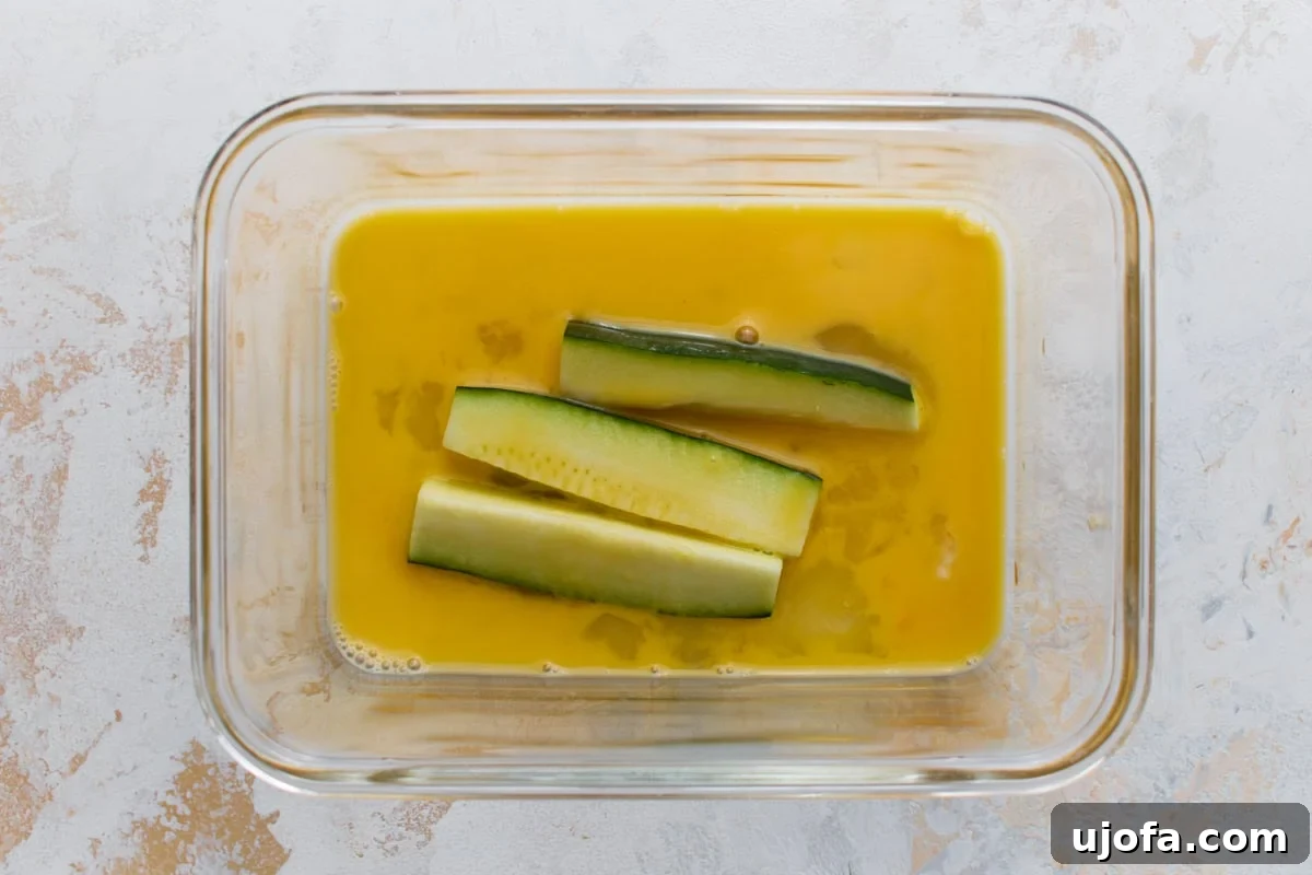 Zucchini sticks dipped in beaten egg before being coated in the Parmesan mixture.