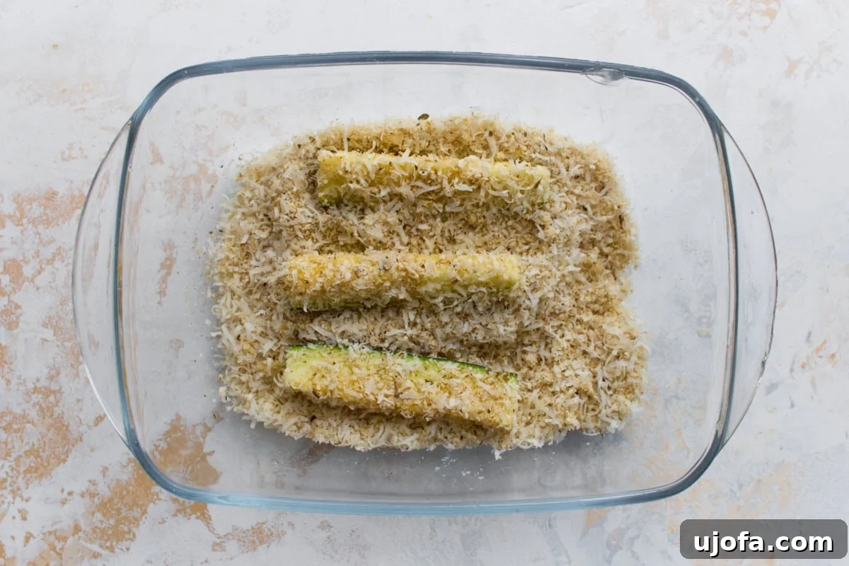 Zucchini fries coated in Parmesan and almond flour breading before baking.