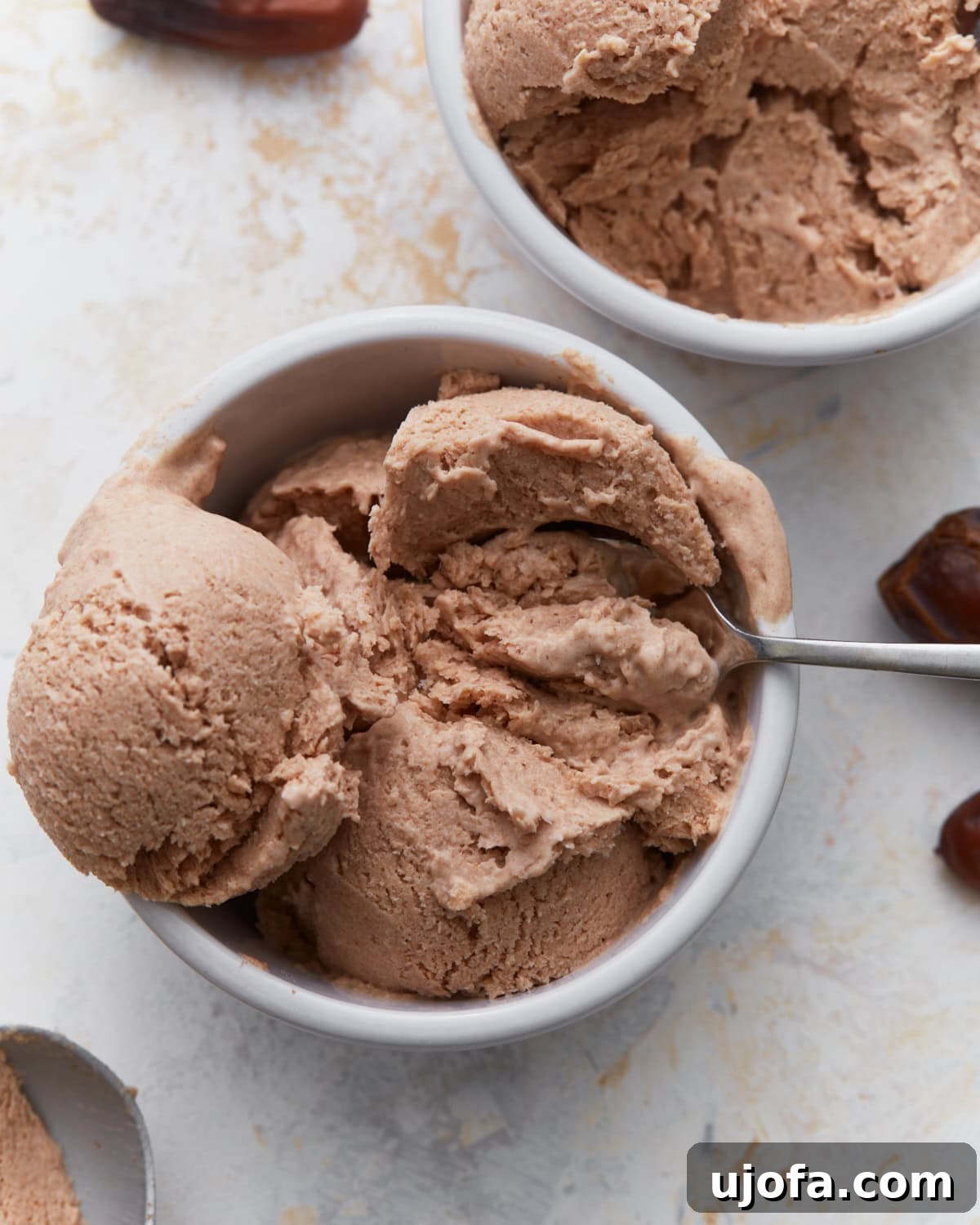 Date ice cream scooped into white bowls with a spoon, showing its creamy texture and caramel-colored appearance.