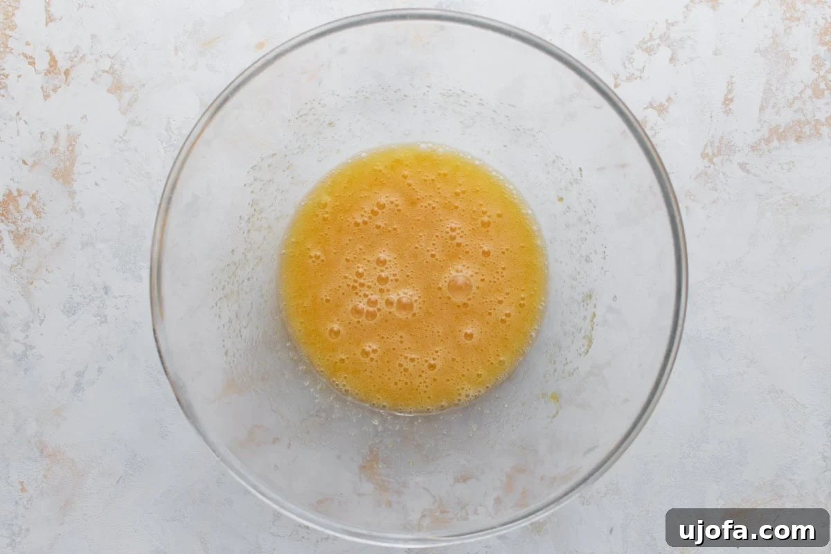 Overhead view of whisked eggs and oil in a glass mixing bowl