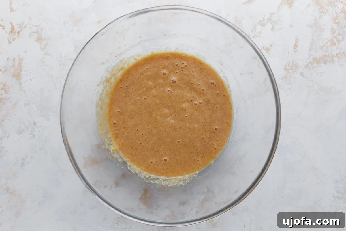 Overhead view of wet and dry ingredients combined into a smooth batter in a glass mixing bowl