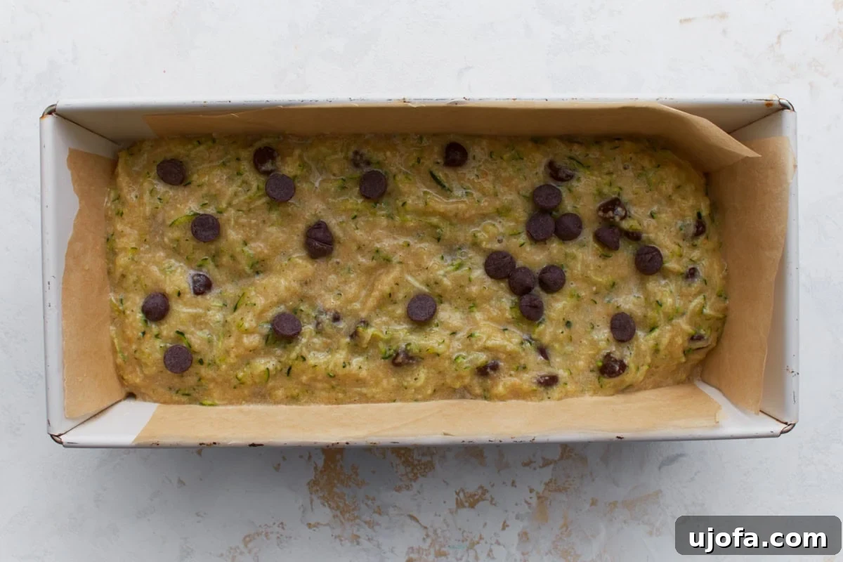 Almond flour zucchini bread batter with chocolate chips poured into a parchment lined loaf pan ready to bake