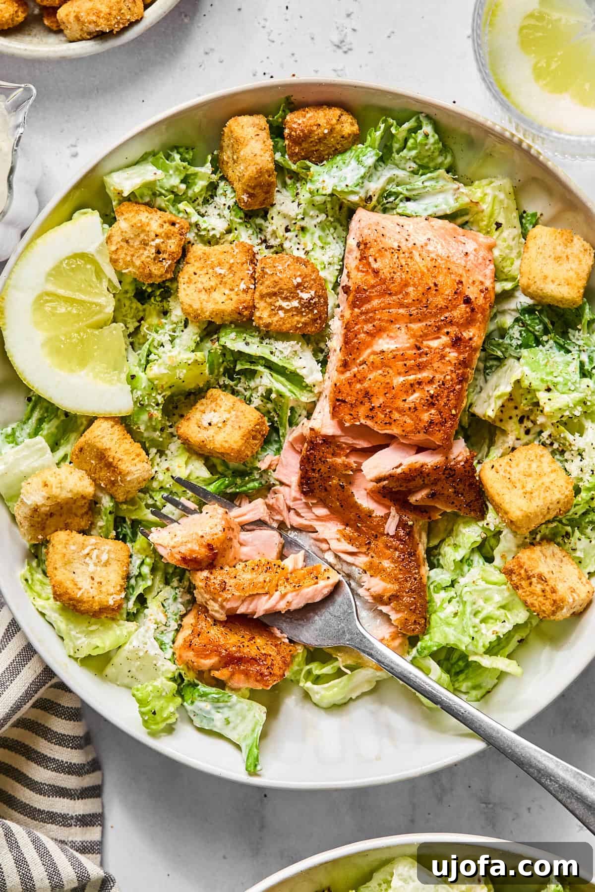 Protein-Packed Salmon Caesar with Creamy Dressing 2 salmon caesar salad in a white bowl with a fork flaking some of the salmon apart