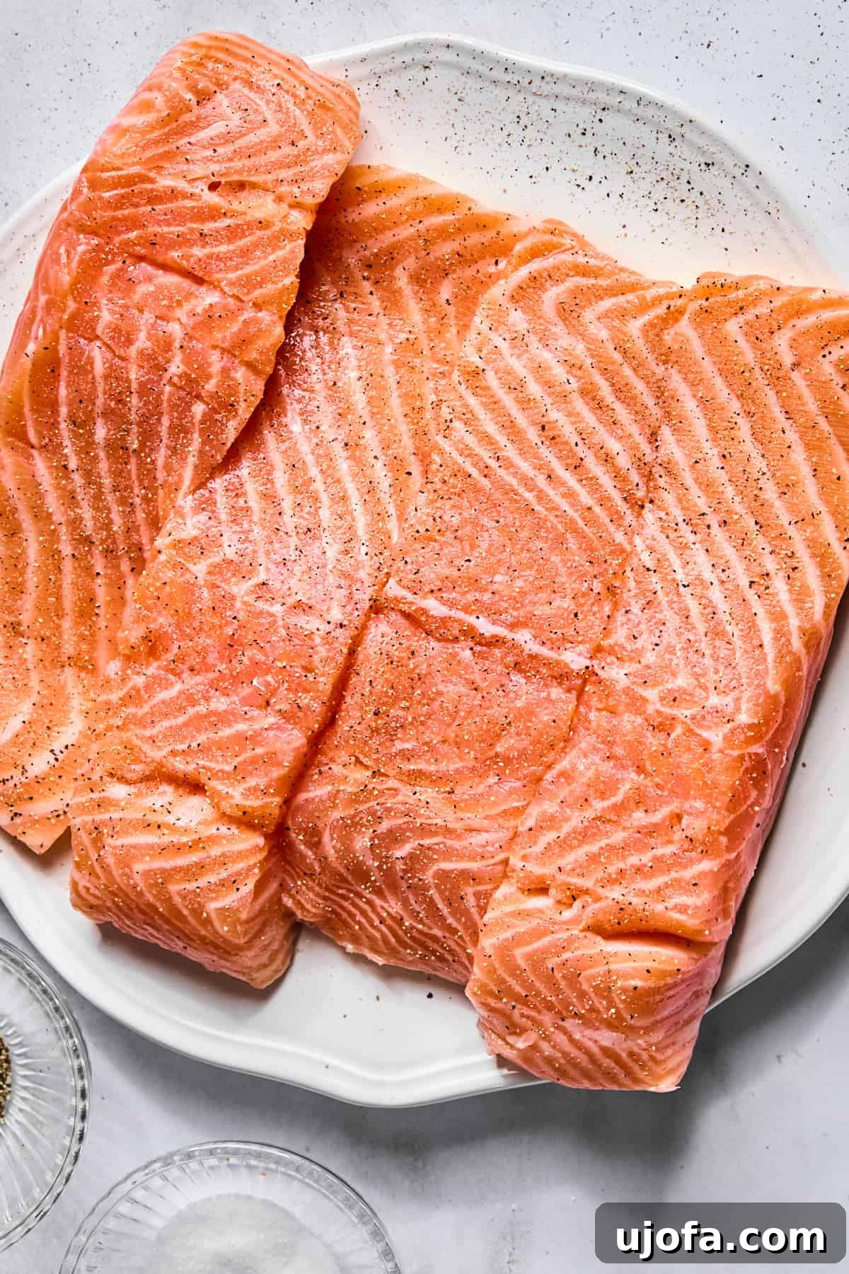 Protein-Packed Salmon Caesar with Creamy Dressing 5 raw salmon fillets on a plate seasoned with salt and pepper
