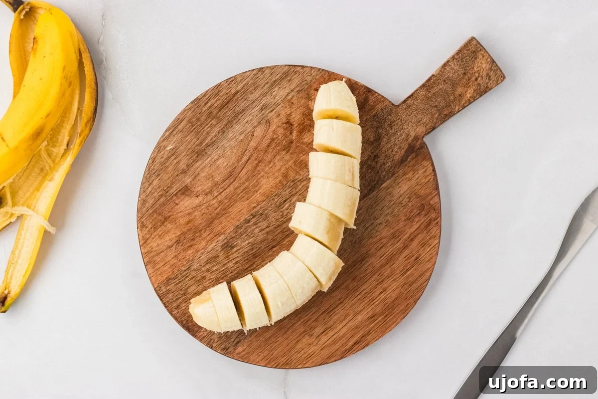 A ripe banana sliced into coins on a round wooden cutting board with the peel set to the side