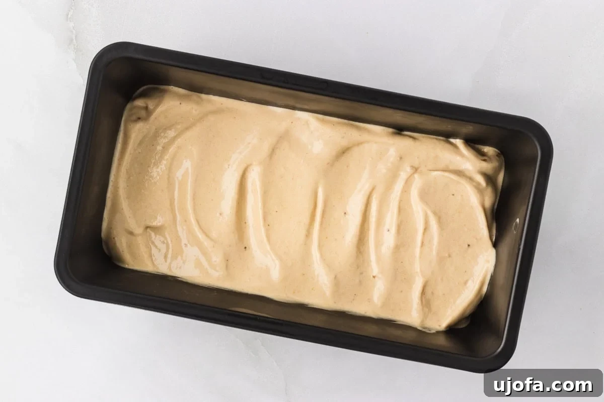 Overhead view of banana peanut butter nice cream mixture transferred and smoothed into a black loaf pan ready to freeze