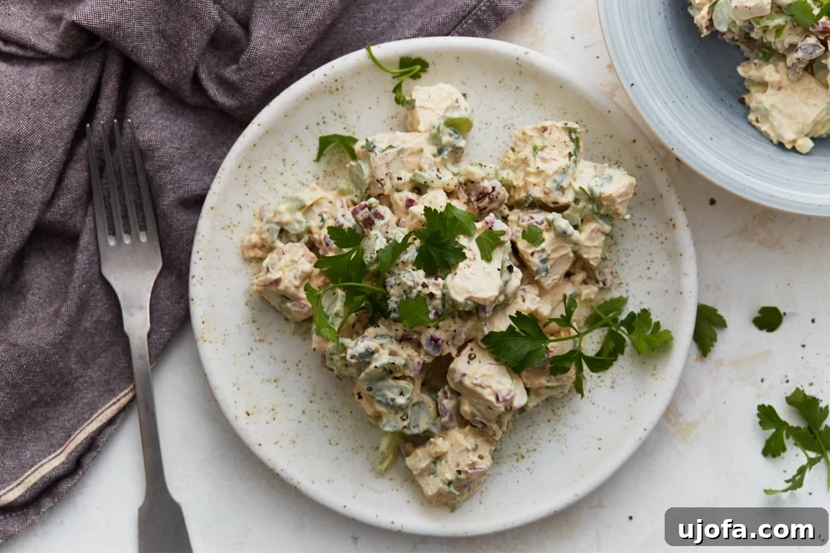 Creamy Keto Chicken Salad with Bacon and Avocado 6 Keto chicken salad served on a white plate with fresh parsley, a fork, and a purple napkin, with a second bowl of salad in the background.