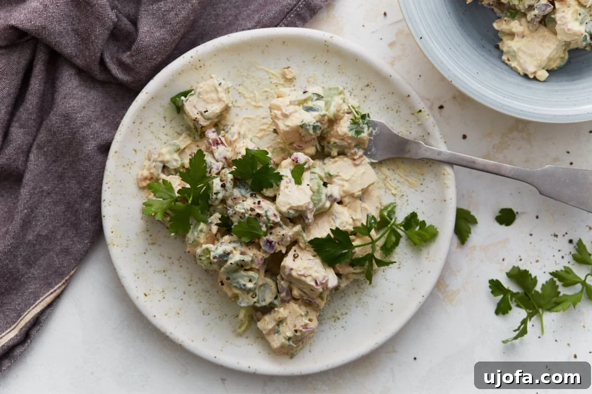 Creamy Keto Chicken Salad with Bacon and Avocado 7 Close-up of keto chicken salad on a white plate with a fork resting beside it, garnished with fresh parsley.