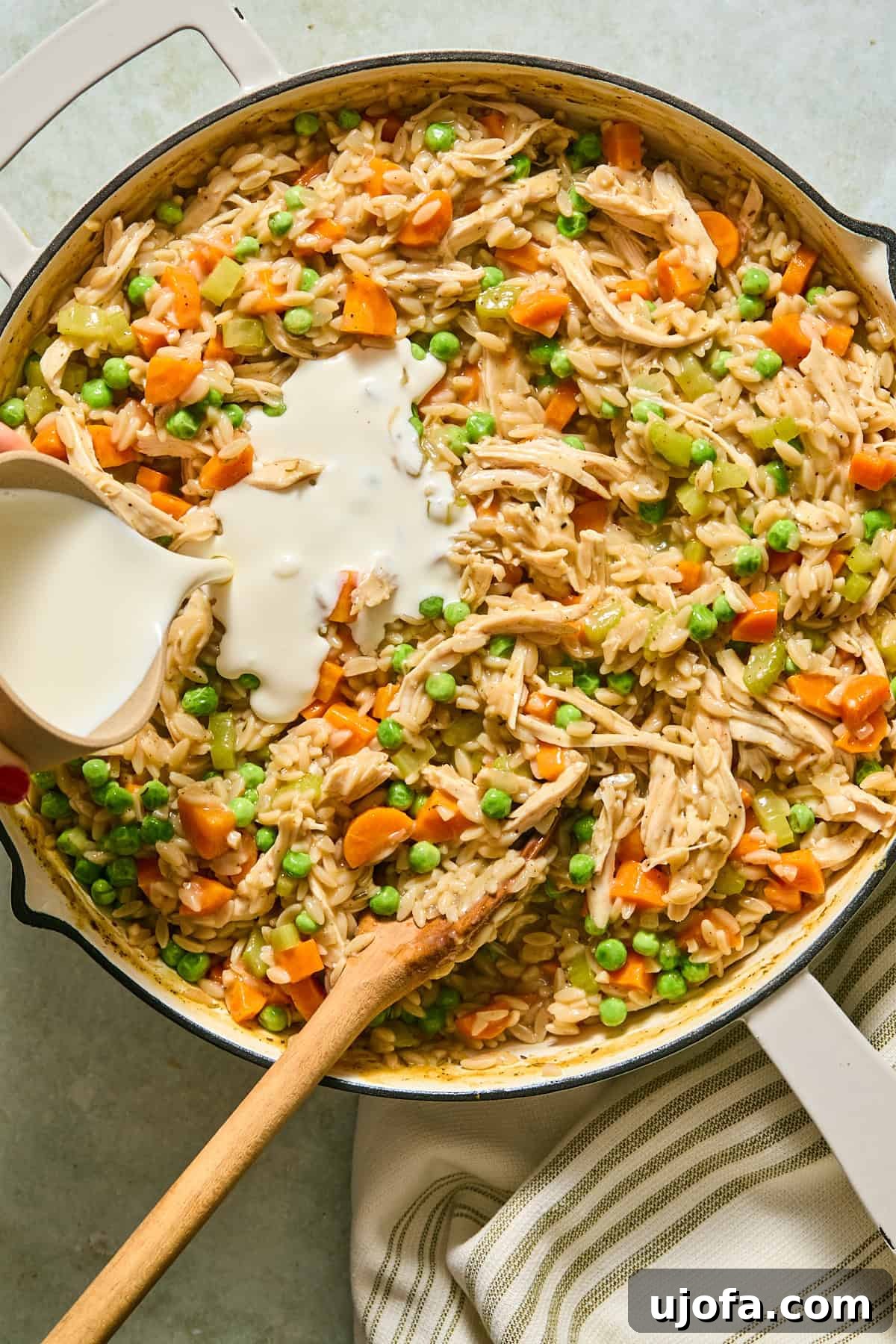 One-Pan Chicken Pot Pie Orzo 9 Half-and-half being stirred into the chicken and orzo mixture, creating a thick and creamy pot pie texture.