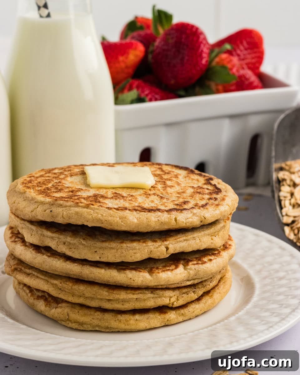Fluffy Oat Flour Pancakes Recipe 2 Stack of oat flour pancakes topped with a pat of butter, served with fresh strawberries and a bottle of milk in the background.