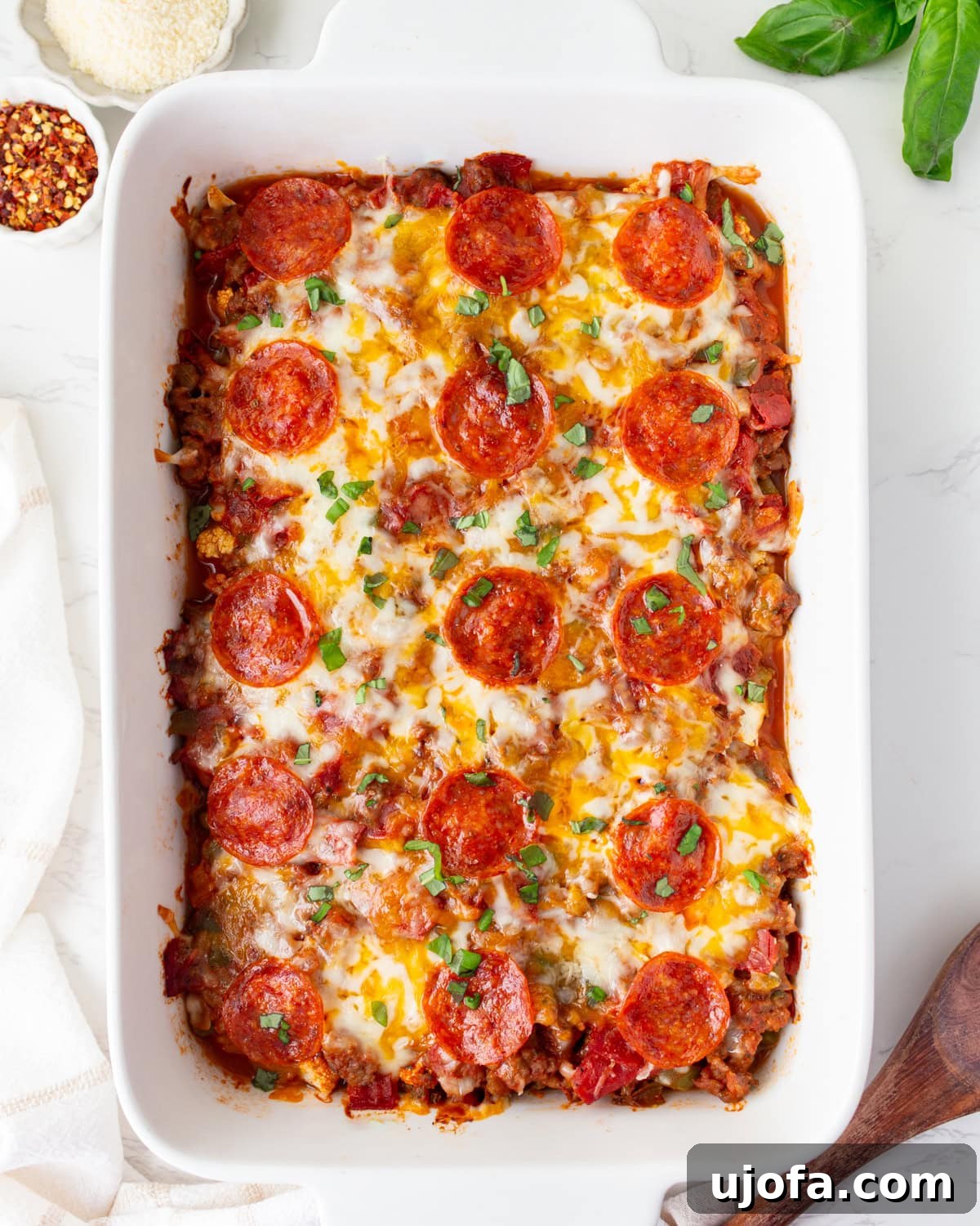 Keto Pizza Casserole: Cheesy Low-Carb Comfort Bake 2 Overhead shot of keto pizza casserole in a white baking dish, topped with melted cheese, pepperoni, and fresh basil.