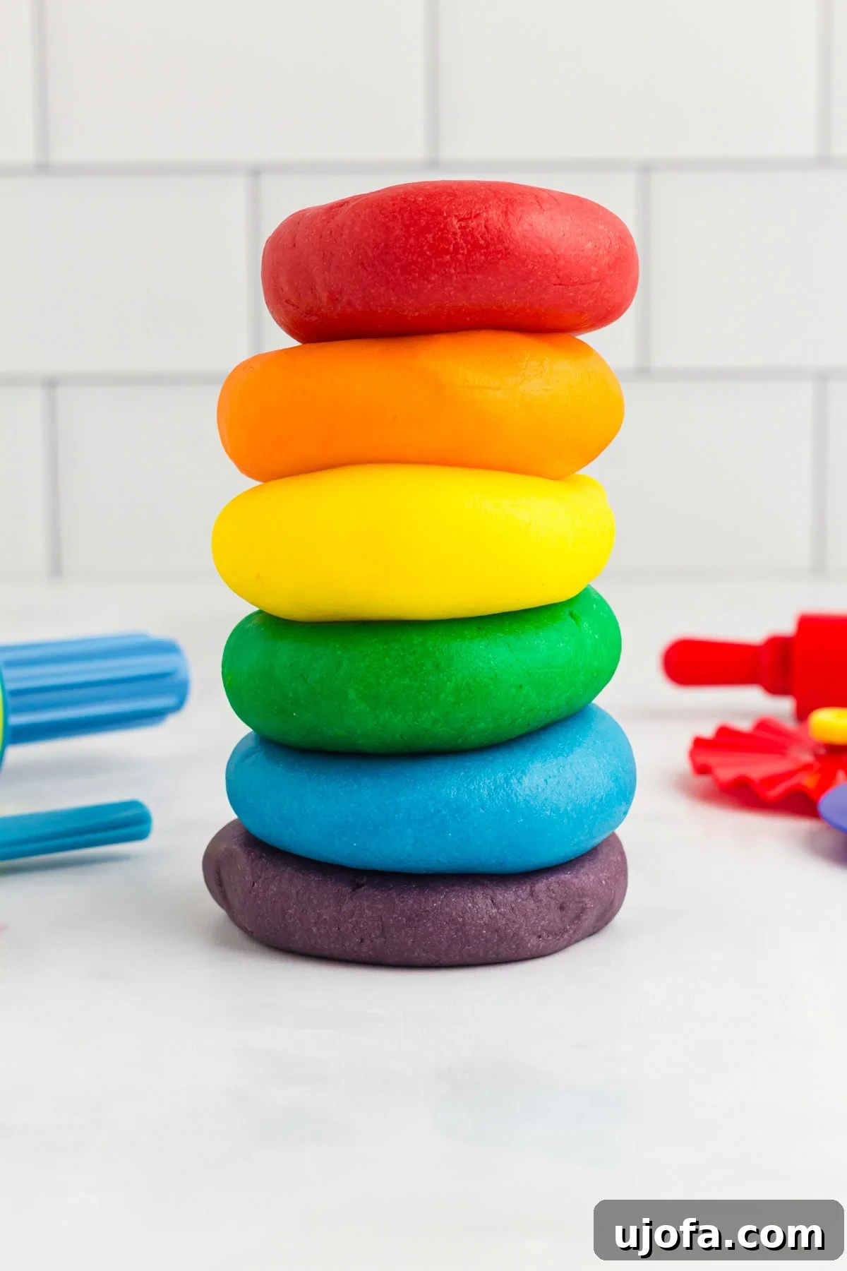 Homemade Gluten-Free Play Dough Recipe for Kids 2 red, orange, yellow, green, blue, and purple play doh stacked on a kitchen counter
