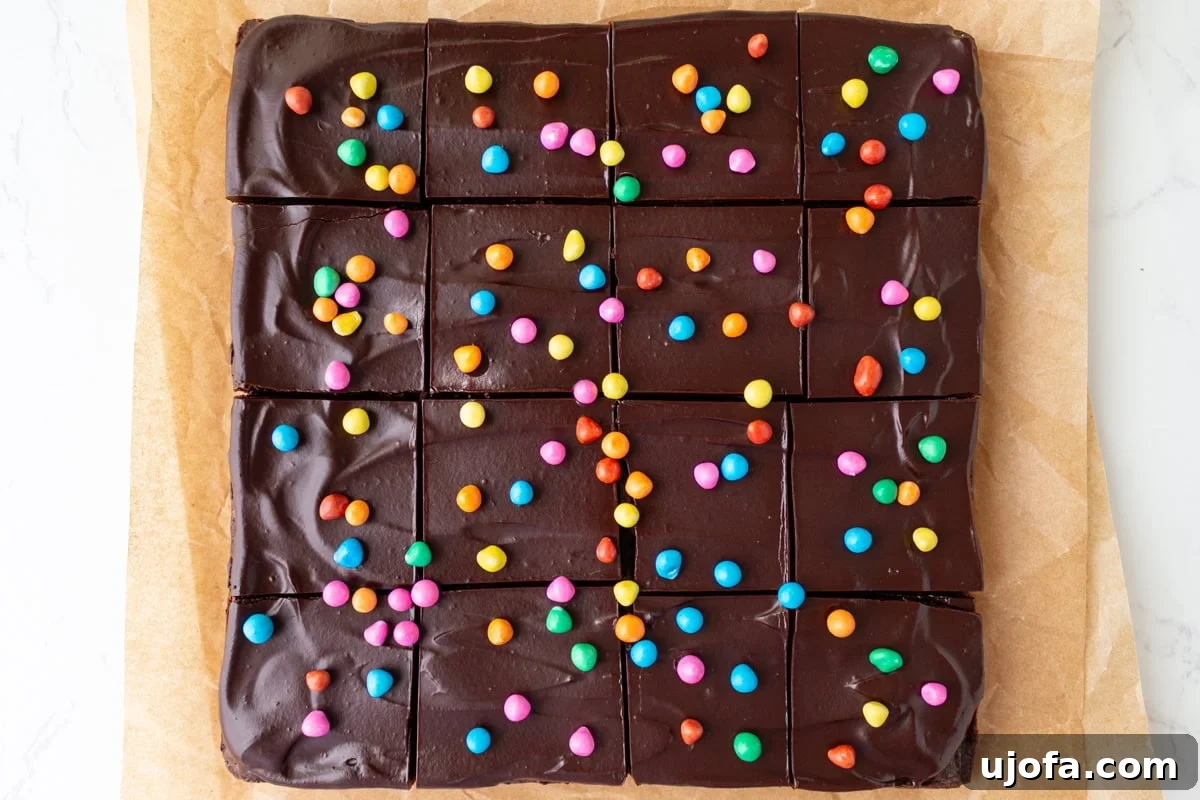 Gluten-Free Cosmic Brownies: Little Debbie Copycat Recipe 10 Frosted gluten-free cosmic brownies cut into squares and topped with rainbow candy chips on parchment paper.